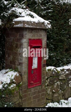 A post box mounted in a wall in a village with snow. during winter. Stock Photo