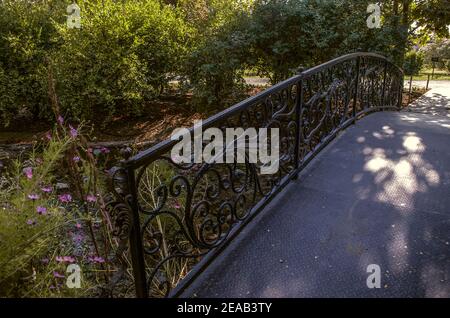 In the shade of trees in a Botanical garden in the suburbs of Tehran on an artificial stream stands an iron bridge with  beautiful wrought iron railin Stock Photo