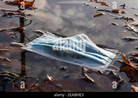 Puddle of water, thrown away mouth and nose protective mask, symbolic photo, environmental pollution, coronavirus, on the wayside in Wilhelmshaven, Lower Saxony, Stock Photo