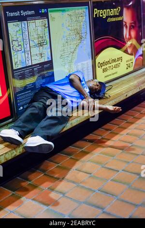 A man sleeps on a bench in the Historic Overtown Metrorail Station in downtown Miami, Florida. Stock Photo