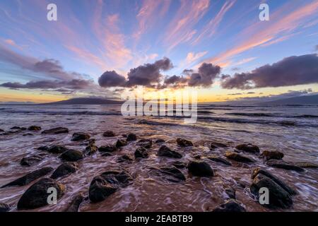 Sunset Rocky Coast - A colorful sunset view at a rocky shore of north-west coast of Maui island, with Lanai island at horizon. Maui, Hawaii, USA. Stock Photo