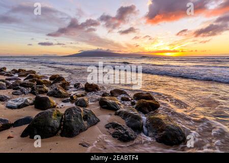 Tropical Sunset - A colorful sunset at a rocky beach of north-west coast of Maui island, with Lanai island at horizon. Hawaii, USA. Stock Photo