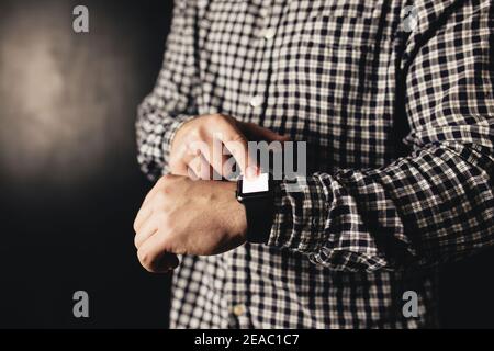 Man in casual clothes clicks hand watches, bracelet, black blurred background Stock Photo