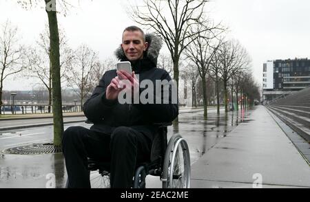 Concept of disabled person. Man in a wheelchair outside in the street. People using technology with smartphone. Stock Photo