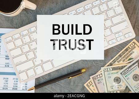 BUILD TRUST is written in a document on the office desk with office accessories, coffee, money and keyboard Stock Photo