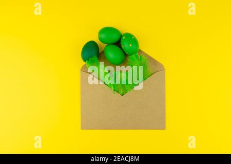 Spring Easter layout with green feathers and eggs, craft envelope on yellow background. Copy space for text for text Stock Photo