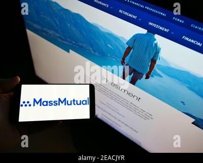 High angle view of person holding smartphone with logo of US insurance company MassMutual on screen in front of web page. Focus on cellphone display. Stock Photo