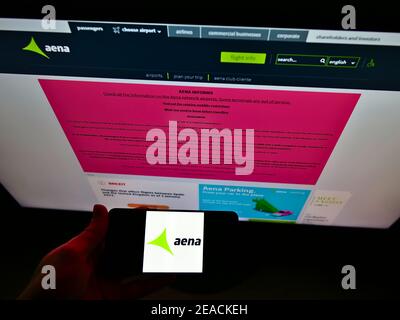 Person holding cellphone with logo of Spanish airport operator Aena S.A. on screen in front of company web page. Focus on smartphone display. Stock Photo