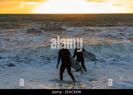 England, East Sussex, Eastbourne, Birling Gap, The Seven Sisters Cliffs and Beach, Two Male Surfers Walking on Beach Carrying Surfboards Stock Photo