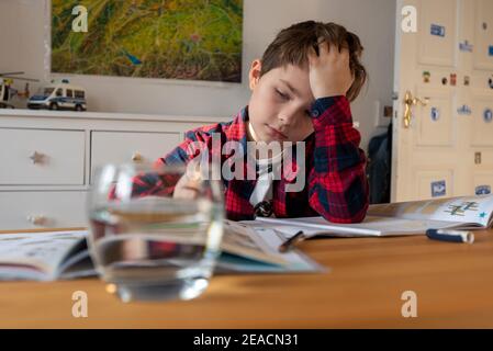 A boy sits at his desk in homeschooling doing chores for school. Stock Photo