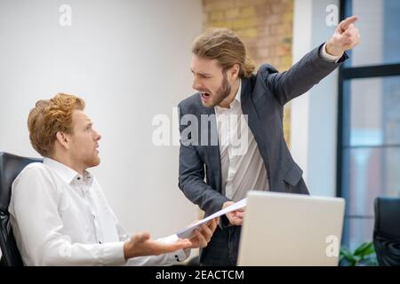 Screaming man pointing with hand and bewildered colleague Stock Photo