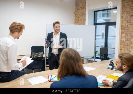 Smiling man showing smartphone and interested colleagues Stock Photo