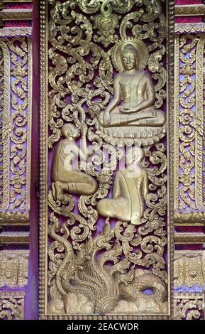 Carved decoration of a dummy window with a Buddha image in Bumisparsa mudra (hand position), Temple Wat Nong Sikhounmuang, Luang Prabang, Laos Stock Photo