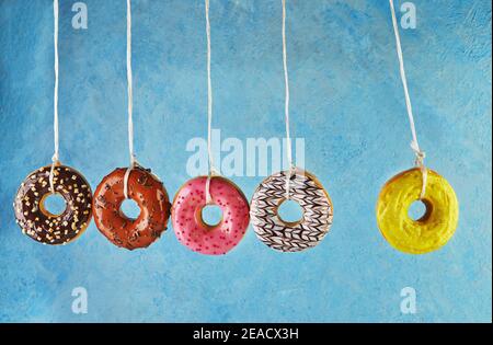 Newton's cradle with multicolored donuts with icing and sprinkles on a blue background. Stock Photo