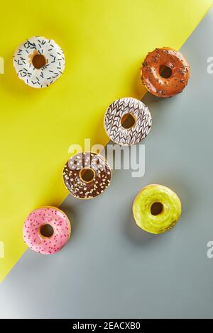 Multicolored donuts with glaze and sprinkles on yellow-gray background. Flat lay Stock Photo