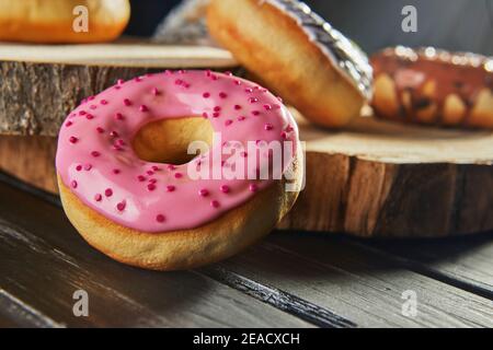 Multicolored donuts with glaze and sprinkles on wooden coasters on a black background. Stock Photo