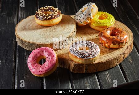 Multicolored donuts with glaze and sprinkles on wooden coasters on a black background. Stock Photo