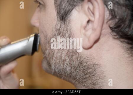 a man shaves his beard with rechargeable machine at home in the pandemic Stock Photo