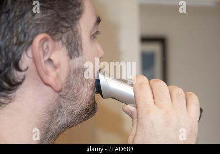 a man shaves his beard with rechargeable machine at home in the pandemic Stock Photo