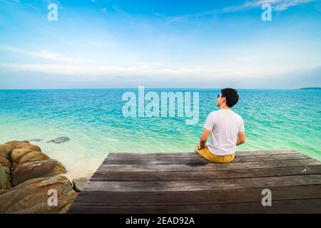 happy man sitting on a wooden bridge in the sea beach at Koh MunNork Island, Rayong, Thailand Stock Photo