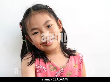 Portrait beautiful child girl with chocolate around her mouth, big smile on cute face, black hair, wearing beautiful pink dress. Beautiful Asian child Stock Photo