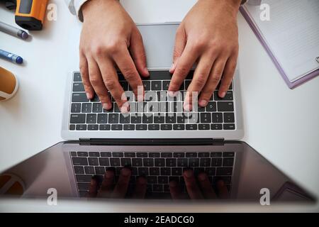 Male hands typing message on laptop on the table in room indoors Stock Photo