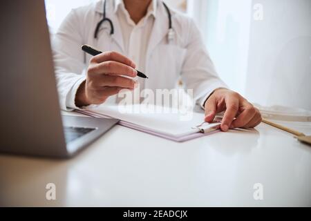 Therapist doing notes on the documents at the work desk with stethoscope on shoulder Stock Photo