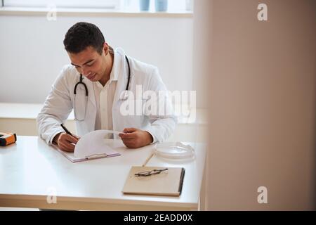 Self confident man doctor sitting at the desk while working with documents in cabinet Stock Photo