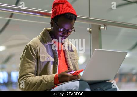 African American traveler millennial man resting and sitting on the floor in airport using cellphone Stock Photo