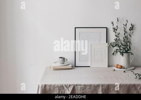 Spring, Easter breakfast still life. Cup of coffee, books and empty picture frames mockups. Linen tablecloth. Olive tree branches in ceramic jug. Hen Stock Photo