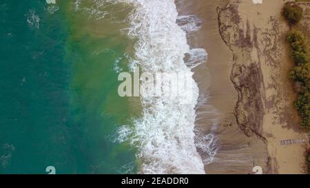 Aerial view of beautiful waves crashing on the sand creating foam, Greece