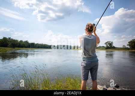 A man fisherman on the river bank throws a fishing pole Stock Photo - Alamy
