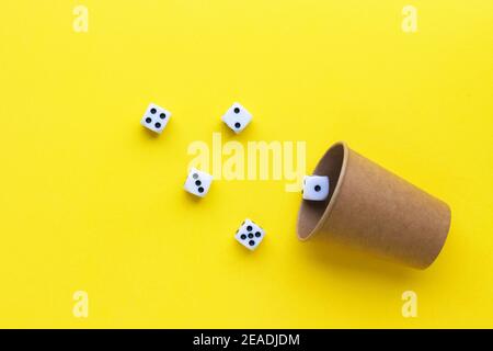 Gaming dice and cardboard cup on yellow background. Playing cube with numbers. Items for board games. Flat lay, top view with copy space. Stock Photo