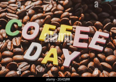 Coffee Day alphabets form on roasted coffee beans background. Stock Photo