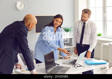 Cheerful girl points to a laptop screen to her excited colleagues in a bright modern office. Stock Photo