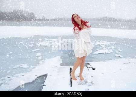 Happy woman hardening and winter swimming concept. Barefoot female enjoying cold snowy weather on an icy lake