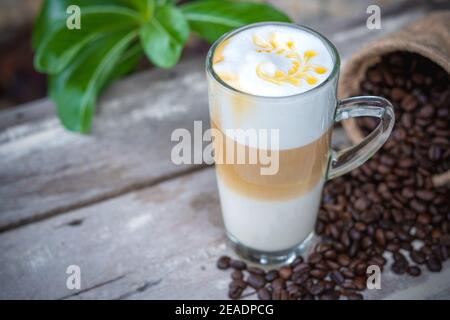 Hot caramel coffee in glass with coffee beans on wooden table background. Stock Photo