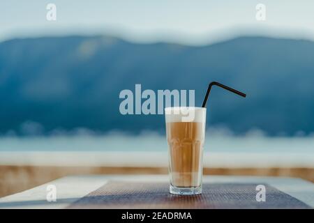Faceted glass with coffee latte and a straw on a blue background. Empty space for text. Stock Photo
