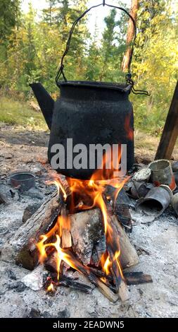 Over the fire hangs an old camp kettle, black with soot and burning. teapot on the fire Stock Photo