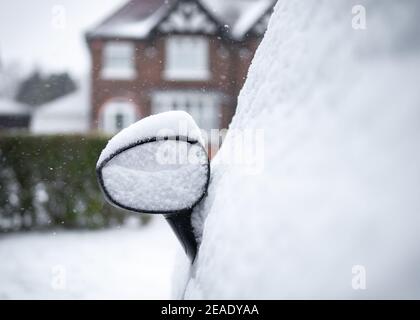 Car mirror parked on drive snowed in heap of snow settled on top house in background on residential street Stock Photo