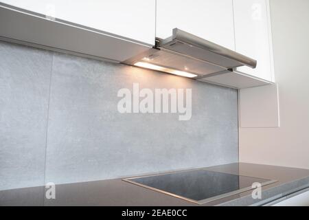 A close-up on under cabinet range hood, exhaust vent hood with lights working and modern electric stove, cooktop in gray and white kitchen design. Stock Photo