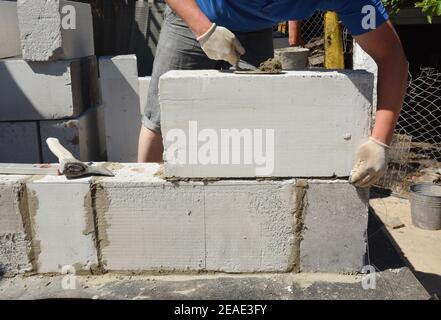 A bricklayer is laying a wall from large gas autoclaved aerated concrete blocks using a trowel and axe. Stock Photo
