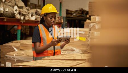 African female warehouse worker using a tablet to check stock in boxes Stock Photo