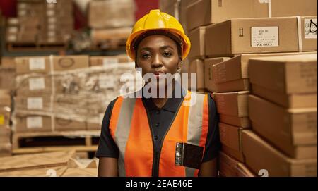Young African female warehouse worker standing by stacks of boxes Stock Photo