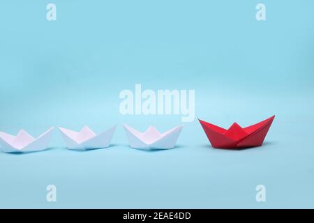 Leadership concept. Blue leader paper ship leading among white on red background Stock Photo