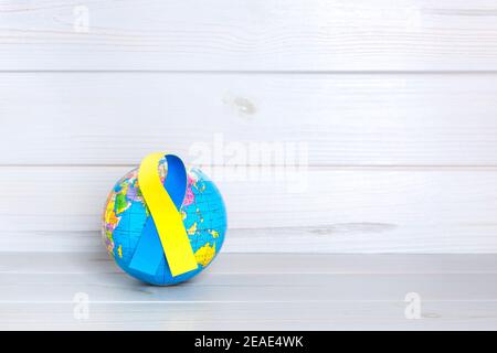 World globe with yellow and blue ribbon on wooden background. World Down Syndrome Day concept. Space for text. Stock Photo
