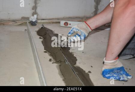 A building contractor is leveling concrete floor using steel beams and plastering after removing them using a spade trowel. Stock Photo