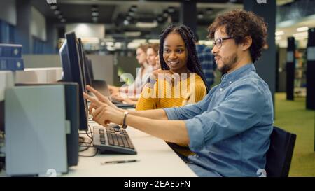 University Library: Bright Black Girl and Smart Hispanic Boy Together Work on Computers, Chat, Discuss Class Assignment, Explain and Advice Each Other Stock Photo