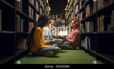University Library: Diverse Group of Students Sitting Cross-Legged On the Floor, Talk, Use Digital Tablet Computer, Share Screen, Have Fun, Discuss Stock Photo