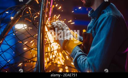 Close Up of a Talented Innovative Artist Using an Angle Grinder to Make an Abstract, Brutal and Expressive Metal Sculpture in a Workshop. Contemporary Stock Photo